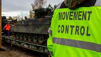 Panzer der Bundeswehr steht am LogHub nach dem Umschlag auf einem Eisenbahnwagen. Davor steht ein Soldat mit Warnweste.