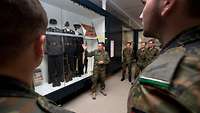 Soldaten sehen sich Exponate (Uniformen) in einer Vitrine an