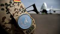 Das Patch der United Nations an der Uniform eines deutschen Soldaten, im Hintergrund ein Flugzeug