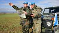 Zwei Soldaten mit blauen Baretts, einer von ihnen macht eine Geste und hält eine Landkarte