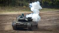Ein Kampfpanzer Leopard 2A7 fährt im Gelände, weißer Rauch steigt auf