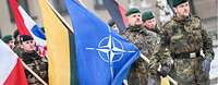 Soldaten unterschiedlicher Nationen marschieren mit Flaggen, ein deutscher Soldat trägt die NATO-Flagge