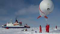 Personen halten in einer Schneewüste einen Helium-Fesselballon