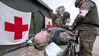 Zwei Soldaten versorgen einen Übungspatienten vor einem Sanitätszelt