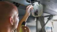 Ein Soldat kontrolliert mit einer Taschenlampe ein technisches Teil eines Kampfflugzeugs vom Typ Eurofighter