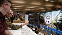 Ein Soldat der Bundeswehr und ein Zivilist sitzen vor Bildschirmen und begutachten digitale Daten