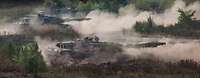 Drei Kampfpanzer vom Typ Leopard umgeben von Rauch im Gelände