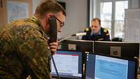 Ein Soldat mit einem Telefonhörer am Ohr telefoniert und schaut auf Computerbildschirme