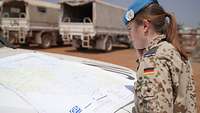 Eine Soldatin mit blauem Barett schaut auf eine Karte, die auf der Motorhaube eines Fahrzeuges liegt