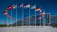 30 Länderflaggen stehen im Kreis um die NATO-Flagge vor einem Gebäude