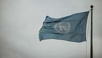 Hinter wolkenbeschlagenem Himmel weht die Flagge der Vereinten Nationen