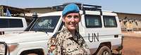 A Portrait of a smiling soldier wearing a blue beret in front an UN vehicle