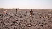 Drei Soldaten gehen während einer Patrouille durch ein Geröllfeld in der Wüste