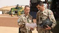 A German soldier and a Romanian pilot stand on an airfield and look at a piece of paper.