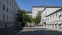 Eine Gruppe von Personen steht vor einer Bronzefigur eines jungen Mannes im Hof des Bendlerblocks.