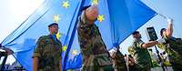 Several soldiers from different nations hoisting a large EU flag during a ceremony