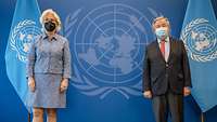Ministerin Lambrecht und Antonio Guterres stehen nebeneinander vor dem Logo und den Flaggen der UN. 