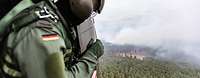 Ein Soldat schaut während des Fluges aus einen Helikopter auf einen Waldbrand.