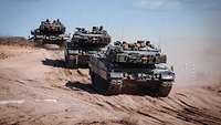 Drei Kampfpanzer vom Typ Leopard fahren auf schwerem Gebiet.