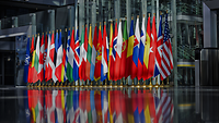 In einem Foyer stehen die Flaggen der Mitgliedsstaaten der NATO nebeneinander aufgereiht.