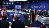 Vor den Regierungschefs und weiteren Personen laufen Soldaten aus den NATO-Staaten und präsentieren ihre Länderflaggen
