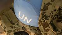 Ein blauer UN-Helm liegt auf Flecktarn-Kleidung.