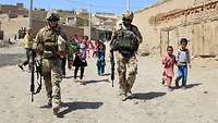 Zwei Soldaten patrouillieren begleitet von einheimischen Kindern durch ein afghanisches Dorf