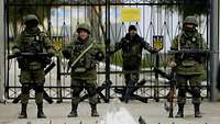 Vier Soldaten ohne Hoheitsabzeichen patrouillieren vor einem Tor