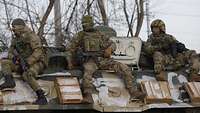 Drei russische Soldaten sitzen in Kampfmontur auf einem gepanzertem Fahrzeug und halten Ausschau