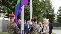 Gemeinsam mit zwei Soldaten hisst die Bundesministerin für Verteidigung die Regenbogenflagge.