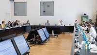 Several persons are seated around a meeting table in a conference room