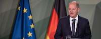 Olaf Scholz steht an einem Rednerpult, dahinter die Flagge Deutschlands und der EU