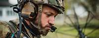 Gesicht eines Soldaten mit Helm und Gehörschutz, er spricht über Funk.