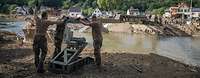 Three servicemen are helping to install a bridge section across a collapsed bridge 