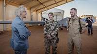 Christine Lambrecht steht mit zwei weiteren Soldaten in einem Hangar, hinter ihnen steht die Drohne Heron 1.