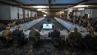 Viele Personen, darunter Politiker und Soldaten verschiedener Nationen sitzen in einem Konferenzsaal in Ramstein.