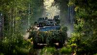 A scout vehicle Fennek drives disguised with branches through a forest, towards the observer.