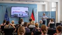 Besucher sitzen bei einem Vortrag im Bundesministerium der Verteidigung, im Vordergrund spricht ein Soldat.