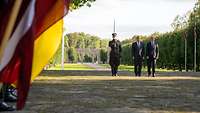 Ein lettischer Soldat, Boris Pistorius und sein Amtskollege Sprūds stehen nebeneinander bei Flaggen