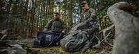 Zwei Soldaten hocken auf Waldboden und sortieren ihre persönliche Ausrüstung in Rucksäcke ein.