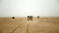 Zwei zivile Fahrzeuge fahren durch staubigen Wüstengrund.