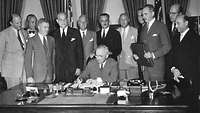 schwarz-weiß Foto: Harry S. Truman unterzeichnet einen Vertrag, um ihn herum stehen weitere Politiker.