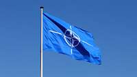 Die Flagge der NATO im Wind vor blauem Himmel.