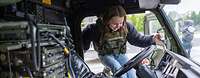 Eine junge Frau mit einer Tarnweste steigt in ein militärisches Fahrzeug.