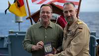 Boris Pistorius und Kommandant einer Fregatte posieren für ein Foto mit Wappen auf Holz in Händen