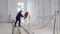Boris Pistorius hängt einen Trauerkranz vor einer weißen Wand mit Inschrift auf