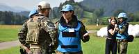 In a staged scene, several soldiers talk to each other, behind them a female soldier comforts a civilian.