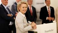 Von der Leyen am Podium, im Hintergrund Männer in Anzügen