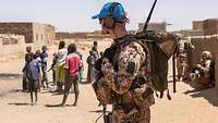 Bundeswehrsoldat mit blauem Basecap läuft auf seiner Patrouille an spielenden Kindern vorbei.