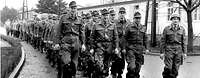 Schwarz-Weiß-Foto: Uniformierte Soldaten in Marschkolonne auf einem Kasernengelände